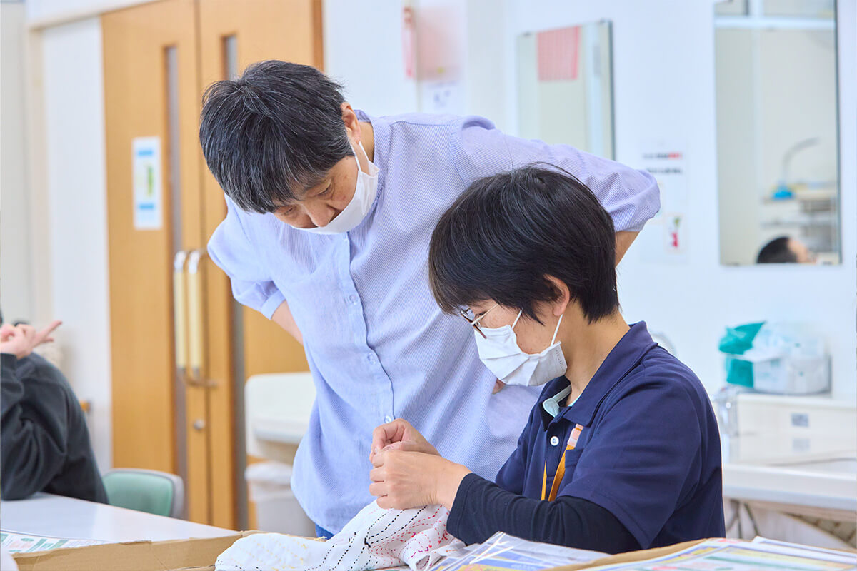 職員が付き添い、利用者が手芸の作業をしている写真
