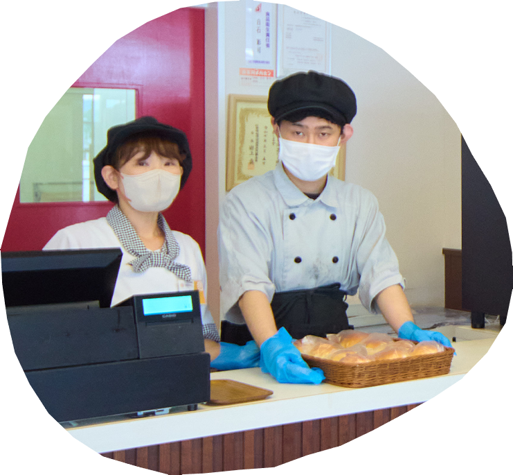 帽子とマスクを着けたスタッフがパン生地を成形している写真